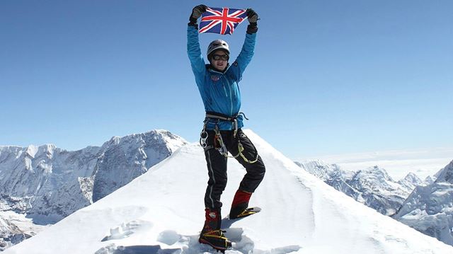 Person standing on top of a snowy mountaintop holding a UK flag